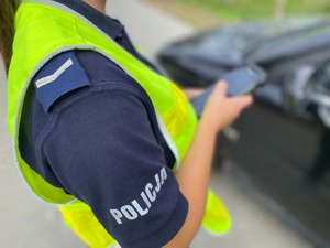 Policjantka stojąca przy samochodzie osobowym z urządzeniem w dłoni